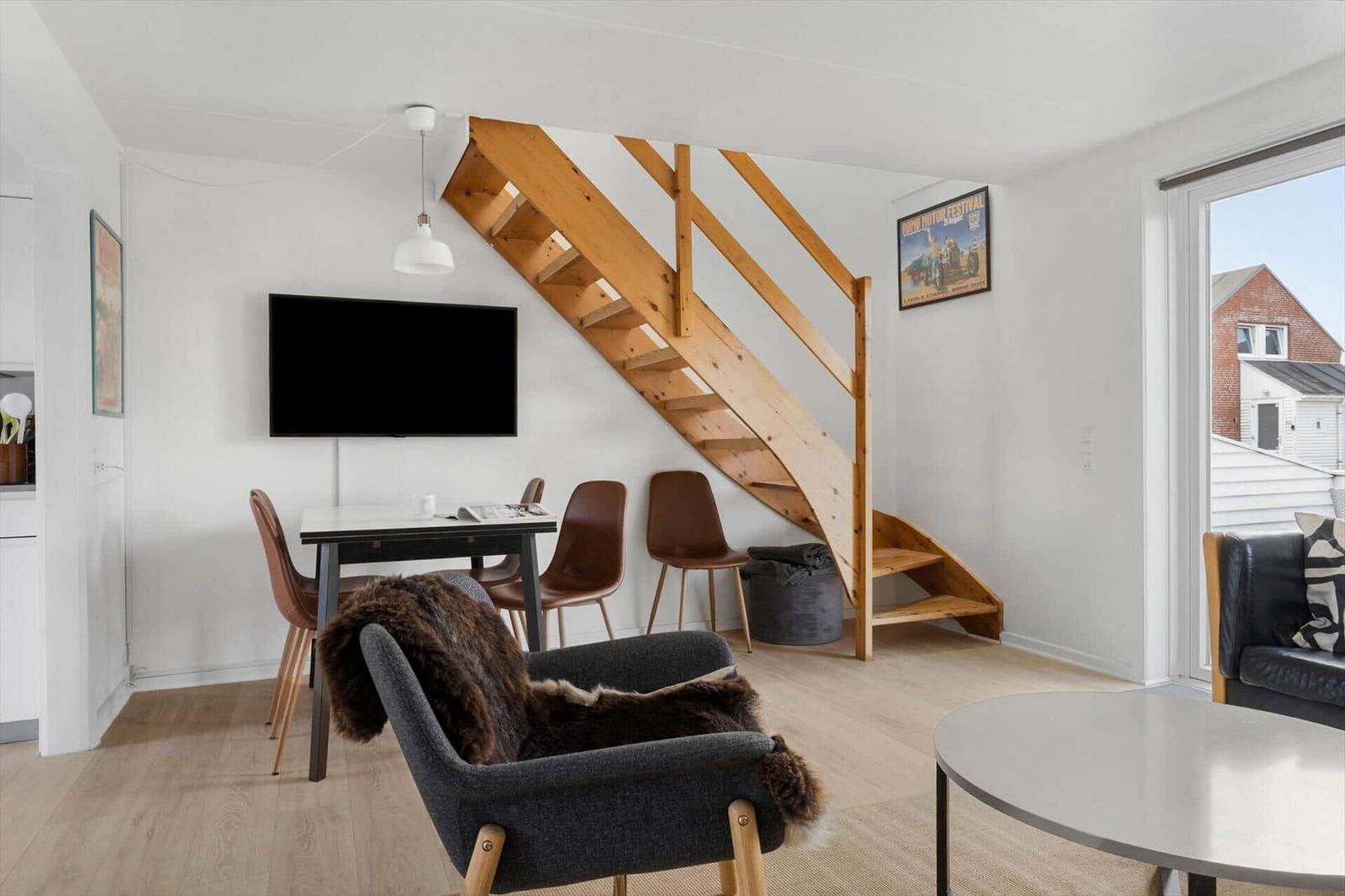 Wohnbereich mit Holztreppe, Esstisch, Sofa und Fernseher an der Wand.