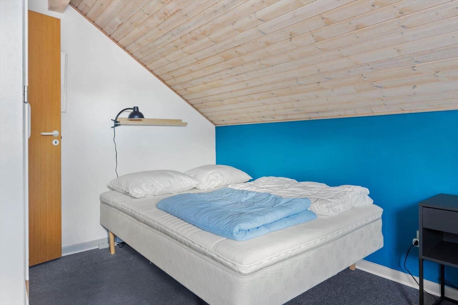Schlafzimmer mit Dachschrägen, blauer Wand und Bett mit Kissen und Decke.