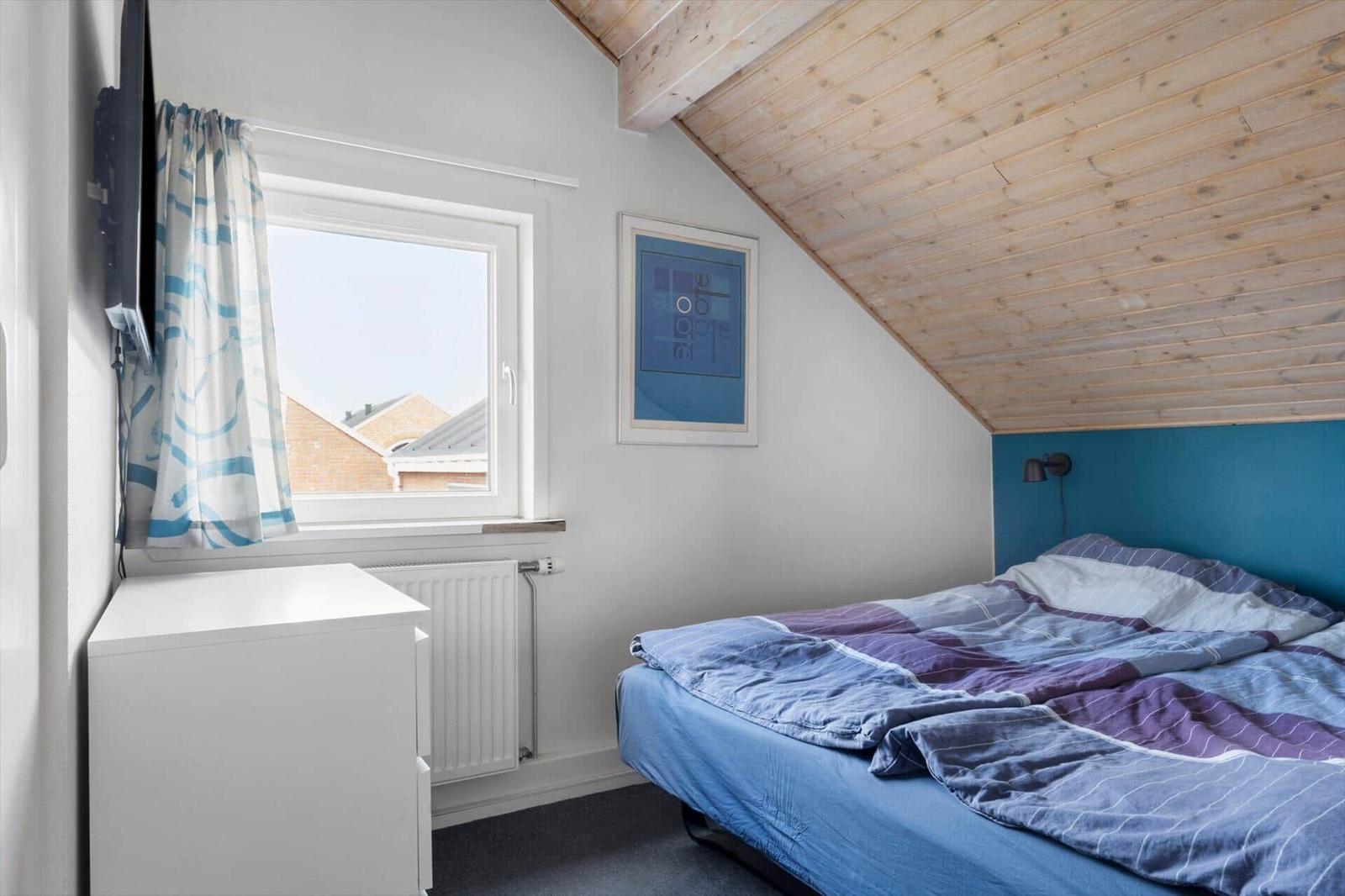 Schlafzimmer mit Bett, Fenster und Holzdecke.