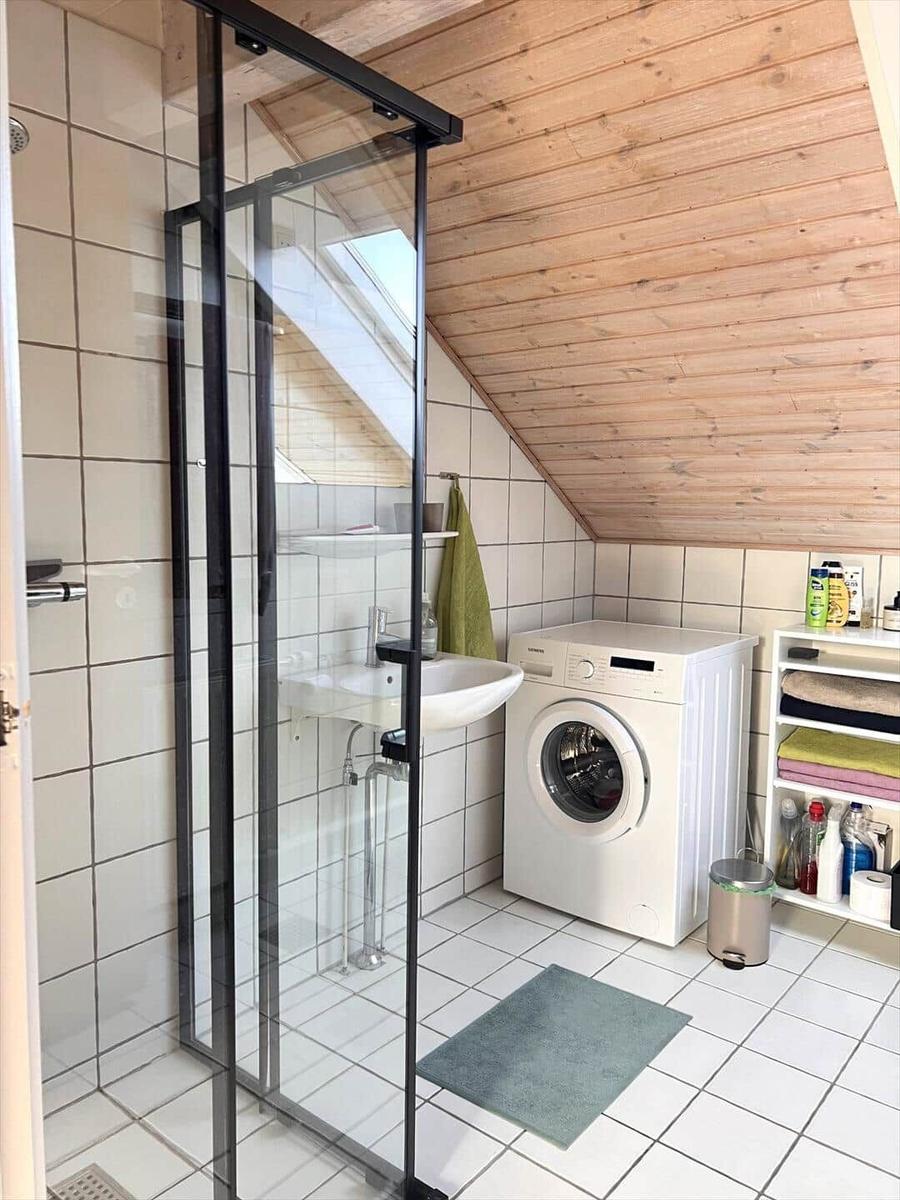 Badezimmer mit Dusche, Waschmaschine und Holzdecke.
