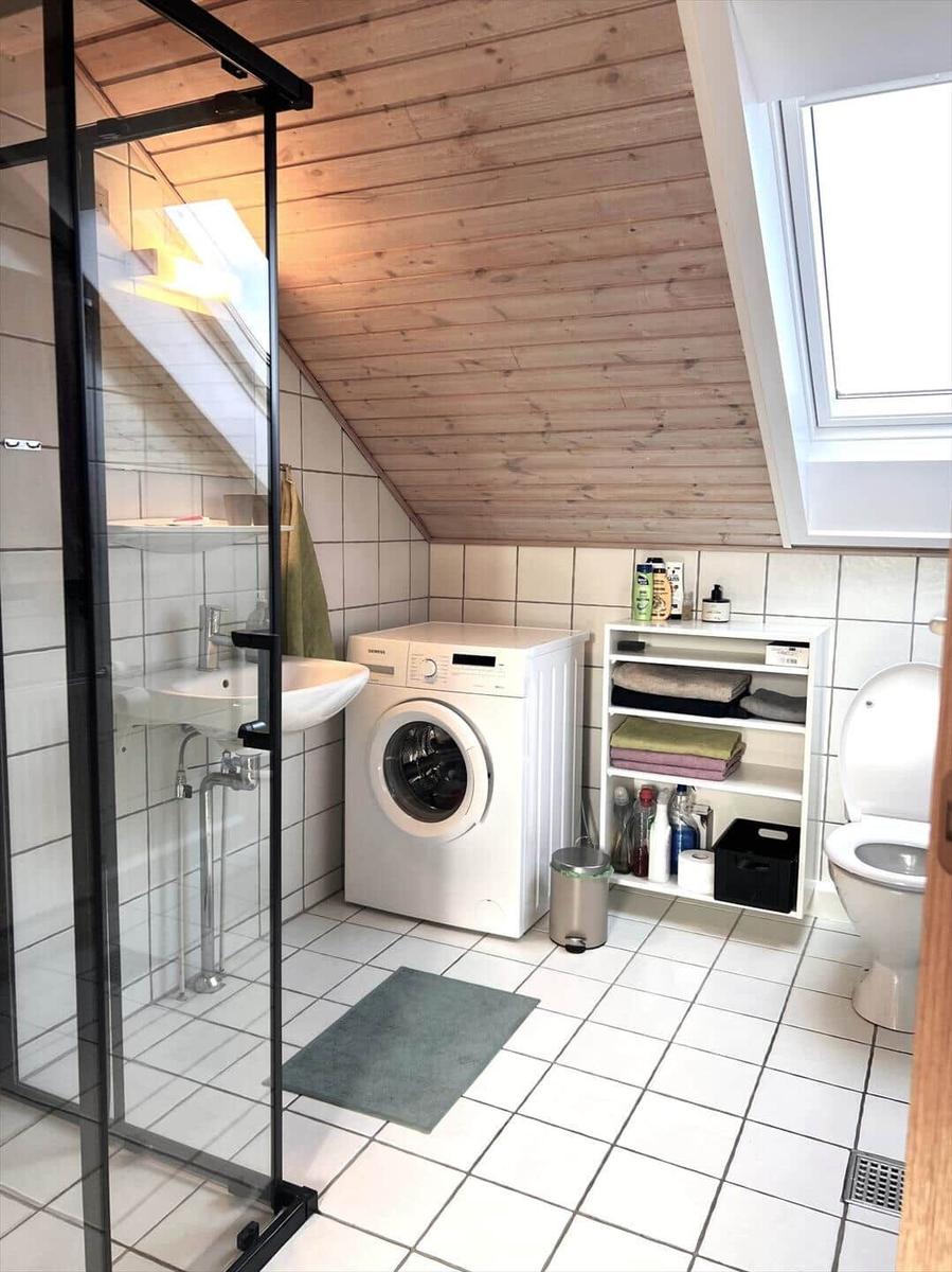 Badezimmer mit Dusche, Waschmaschine und Toilette unter Holzdecke.