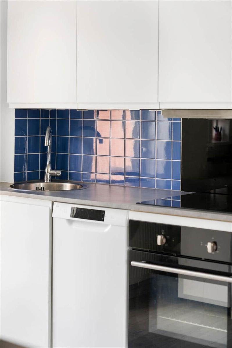 Küche mit weißen Schränken, blauer Fliesenspiegelwand, Edelstahlspüle und integriertem Geschirrspüler.