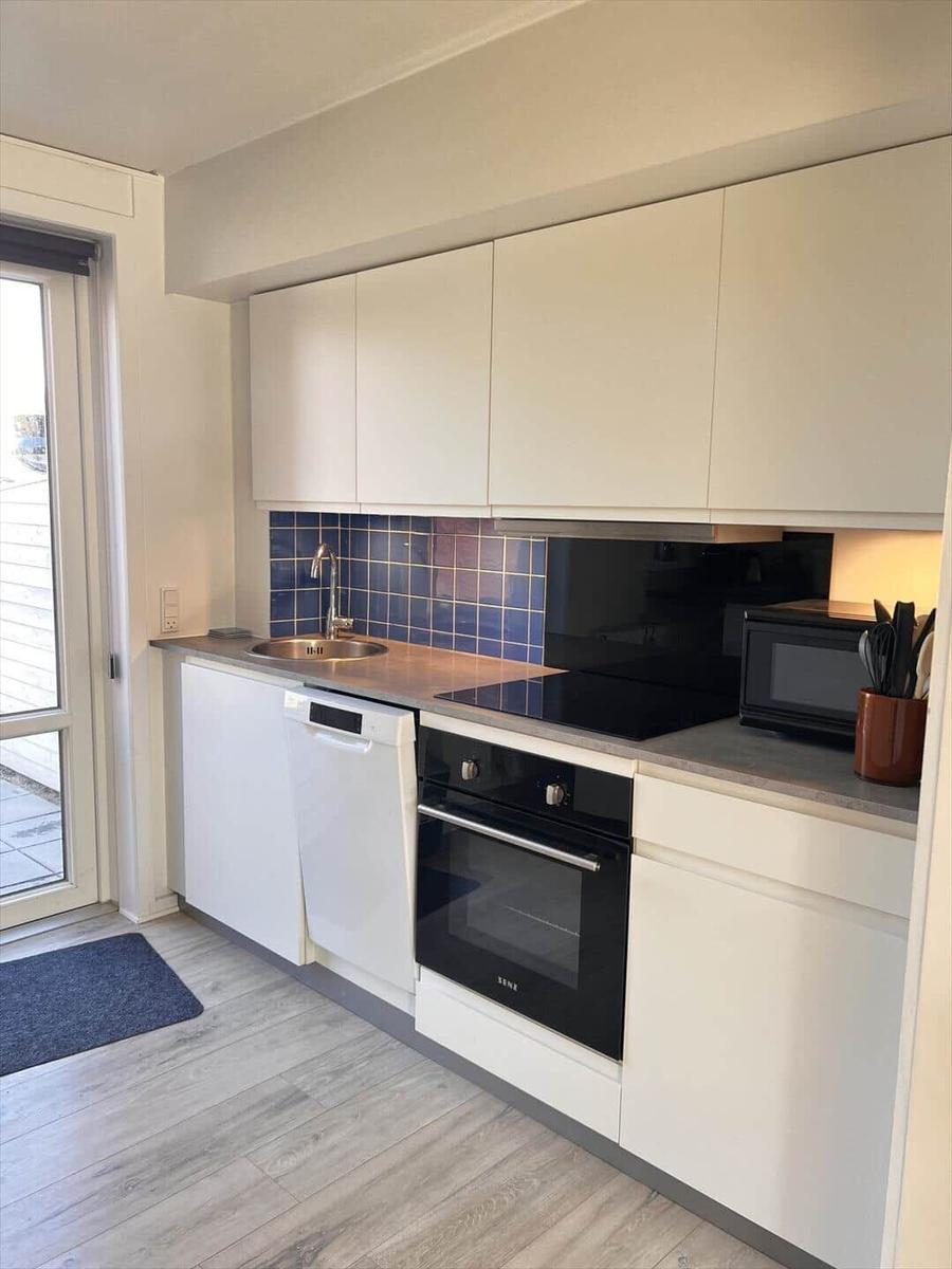 Küche mit weißen Schränken, Edelstahlspüle, Herd und Backofen. Blaue Fliesen an der Wand.