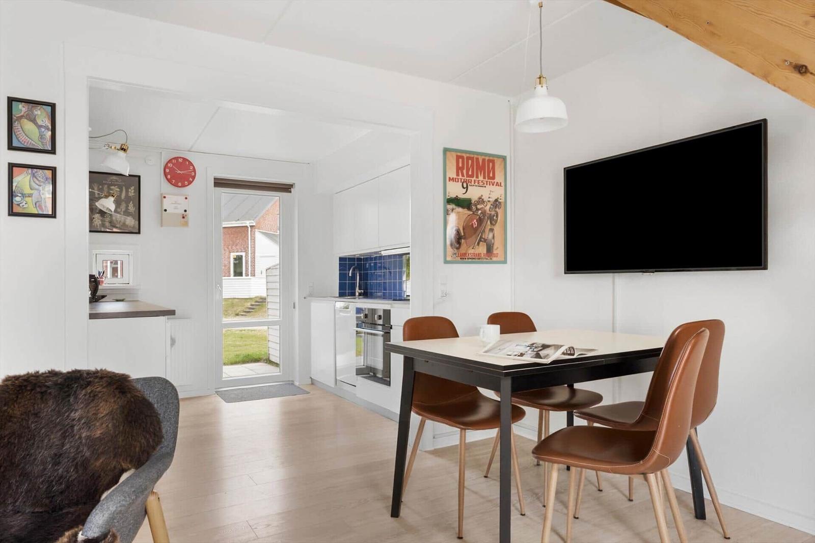 Esszimmer mit Tisch, Stühlen und TV. Küche und Eingangsbereich sind sichtbar.