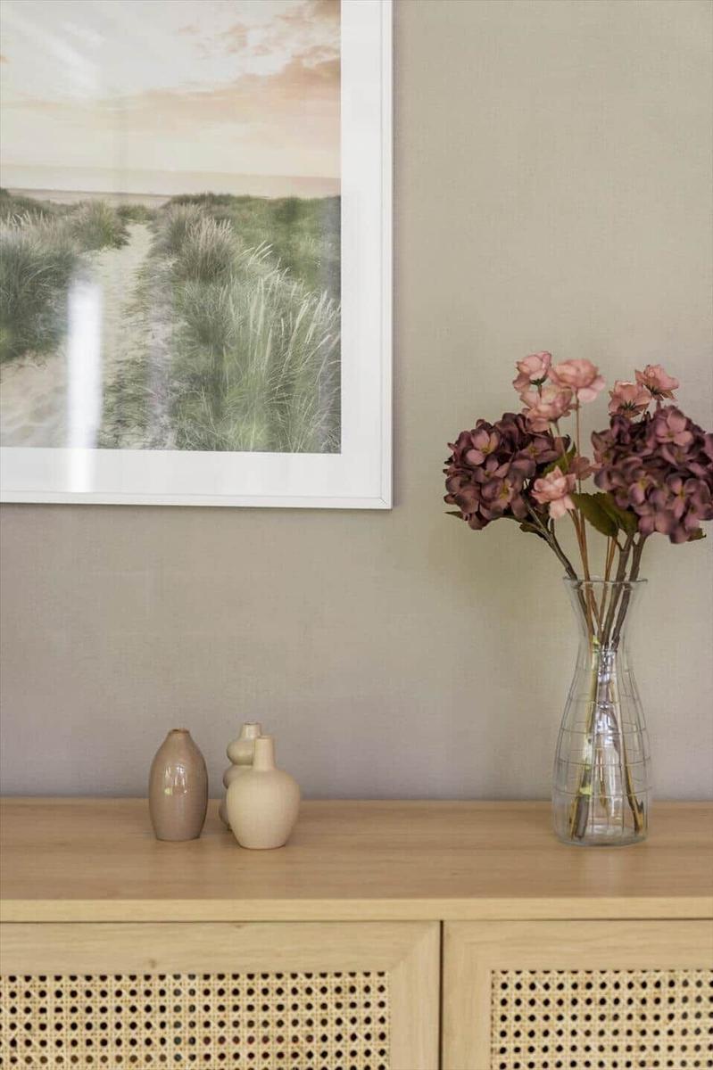 Holzschrank mit Körbchenfront, Vasen und Blumen in einem Raum mit Wandbild.