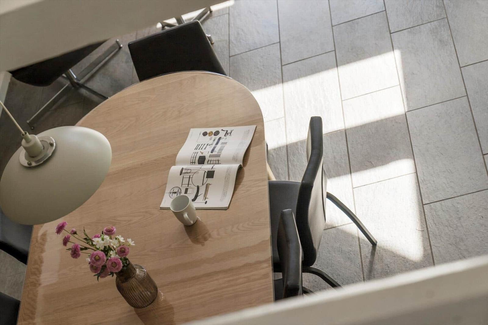 Runder Tisch mit Stühlen, Blumen und Zeitschrift auf Holzoberfläche.