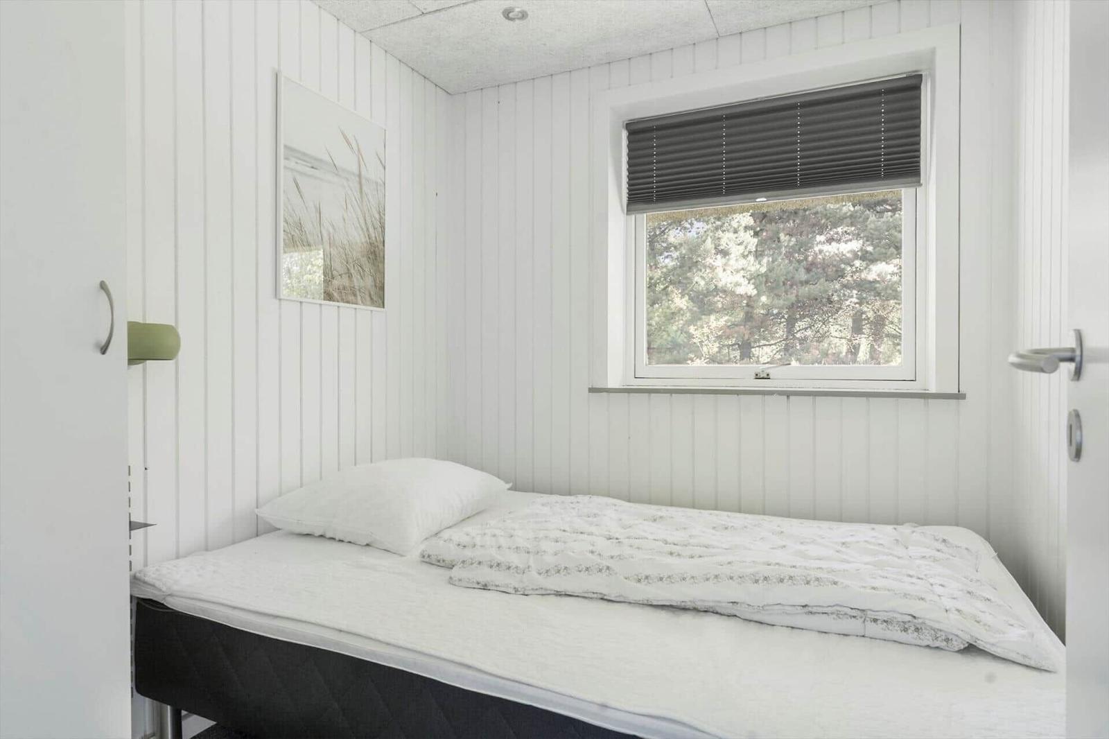 Ein Schlafzimmer mit Bett, Fenster und Wandverkleidung.