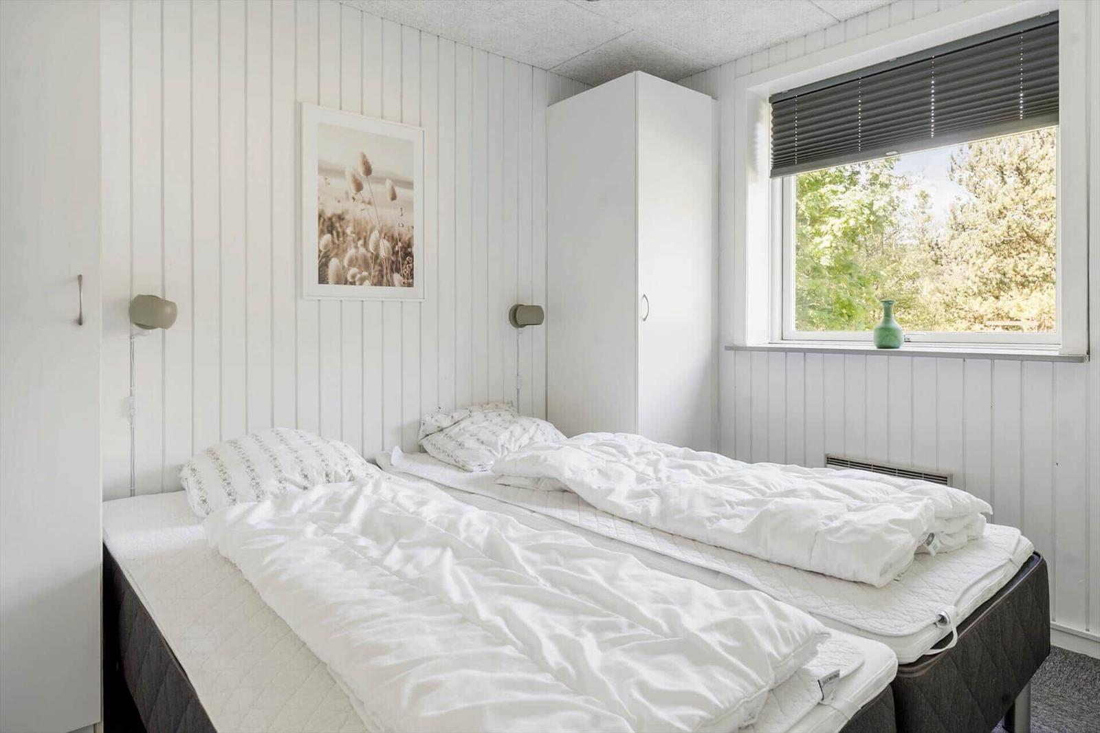 Zwei Betten mit weißen Bettwäschen, Fenster mit Blick auf Bäume und weißer Schrank.