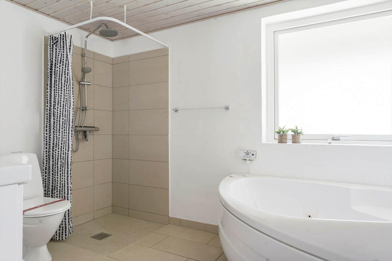 Badezimmer mit Dusche, Badewanne und Toilette. Fenster mit Pflanzen.