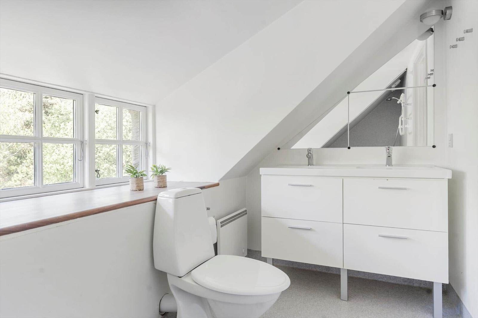 Badezimmer mit Toilette, Waschbecken und Fenster mit Blick auf Grün.