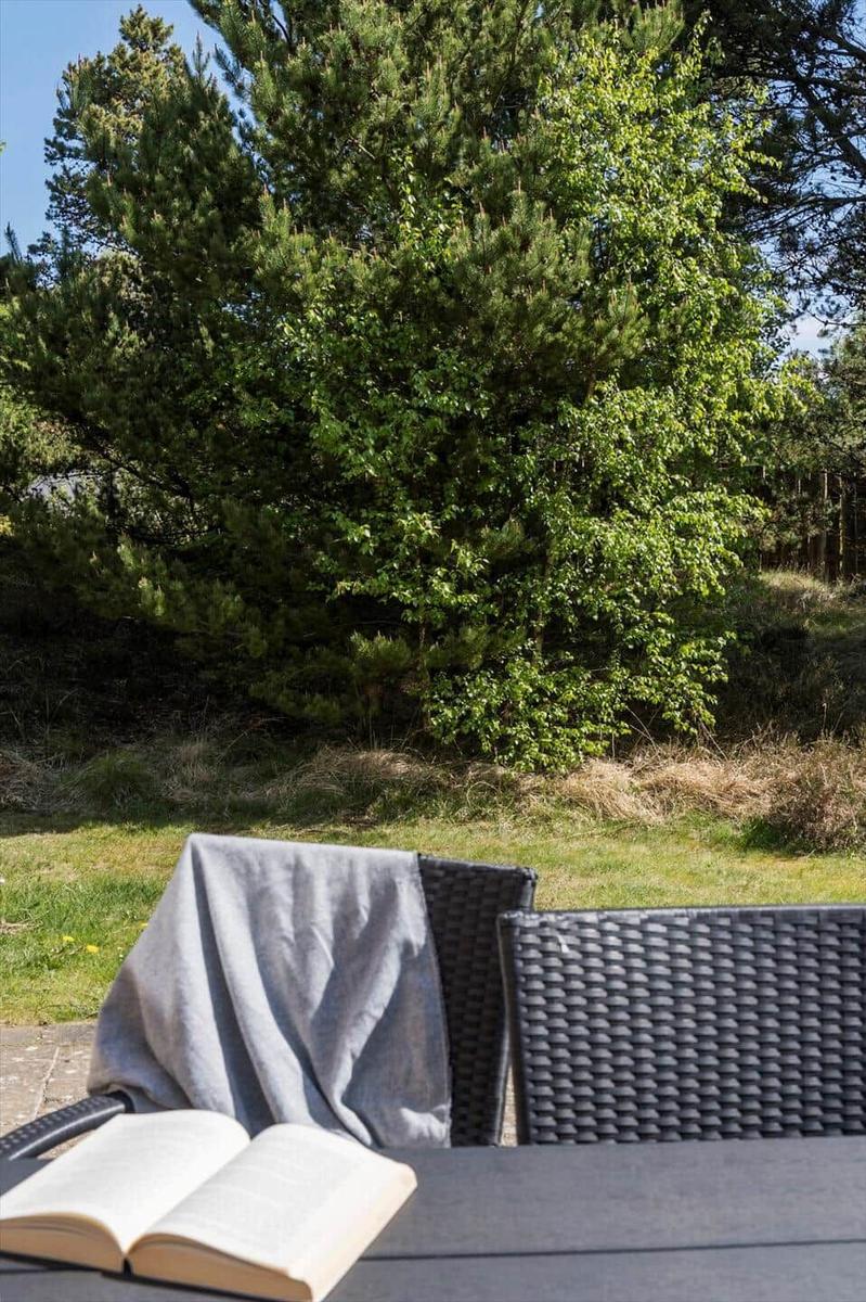 Außenbereich mit Tisch, Stühlen und offenem Buch vor grüner Vegetation.
