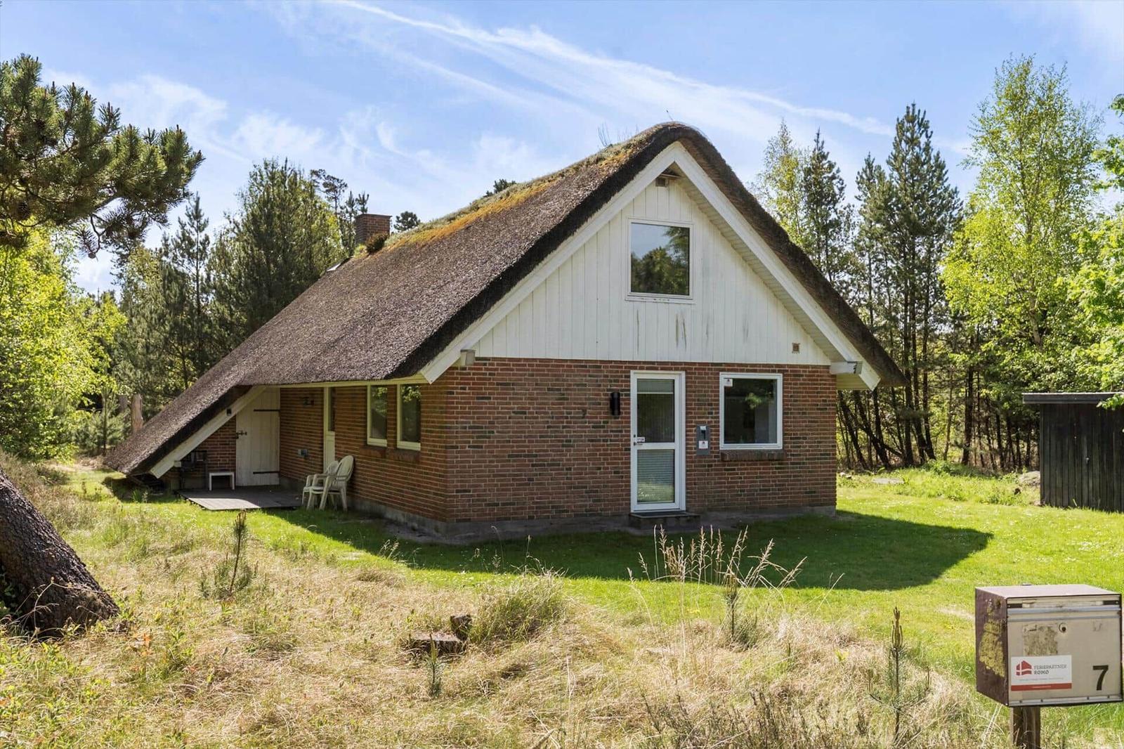 Ein kleines Haus mit strohgedecktem Dach und Backsteinfassade steht inmitten von Bäumen.