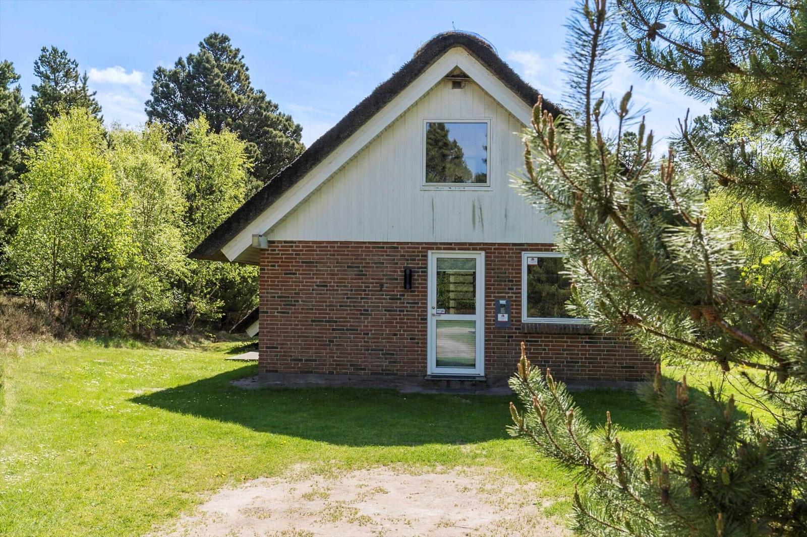 Haus mit Strohdach, Backsteinwand und grünem Garten. Eingangstür und Fenster sichtbar.