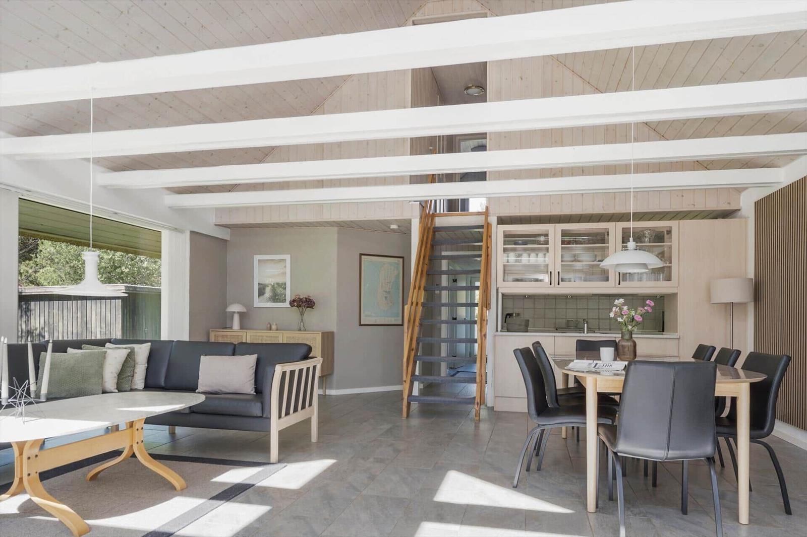 Wohn- und Essbereich mit Holzdecke, Sofa, Tisch und Stühlen. Treppe zur oberen Etage.