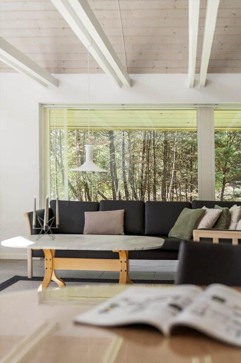 Ein Wohnzimmer mit Sofa, Tisch und Blick auf einen Wald.