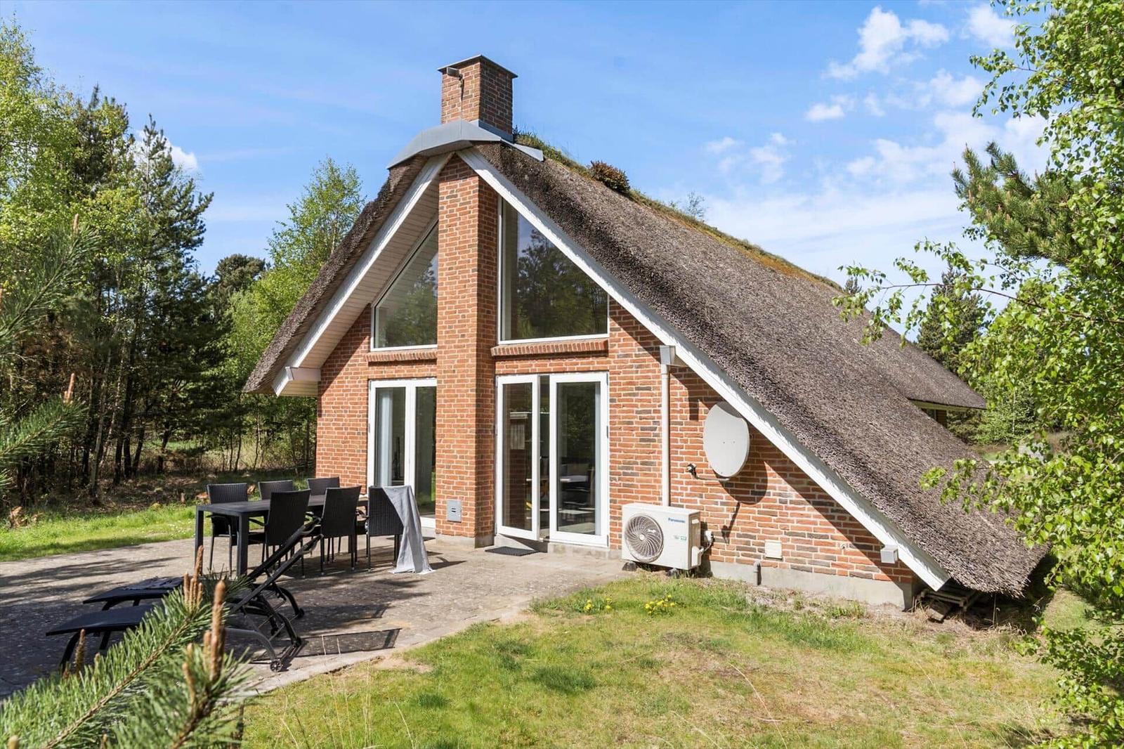 Haus mit strohgedecktem Dach, Terrasse und Garten in Waldnähe.