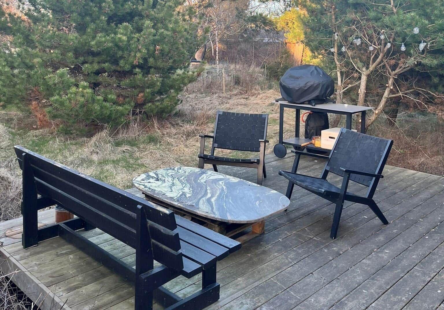 Terrasse mit Tisch, zwei Stühlen und Bank. Grill und Lichterkette im Hintergrund.