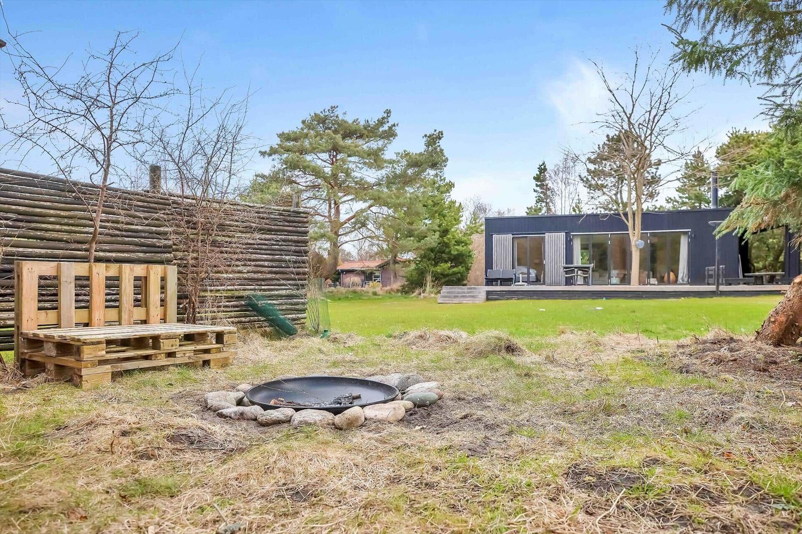 Haus mit großem Garten, Feuerkorb und Holzbank im Freien.