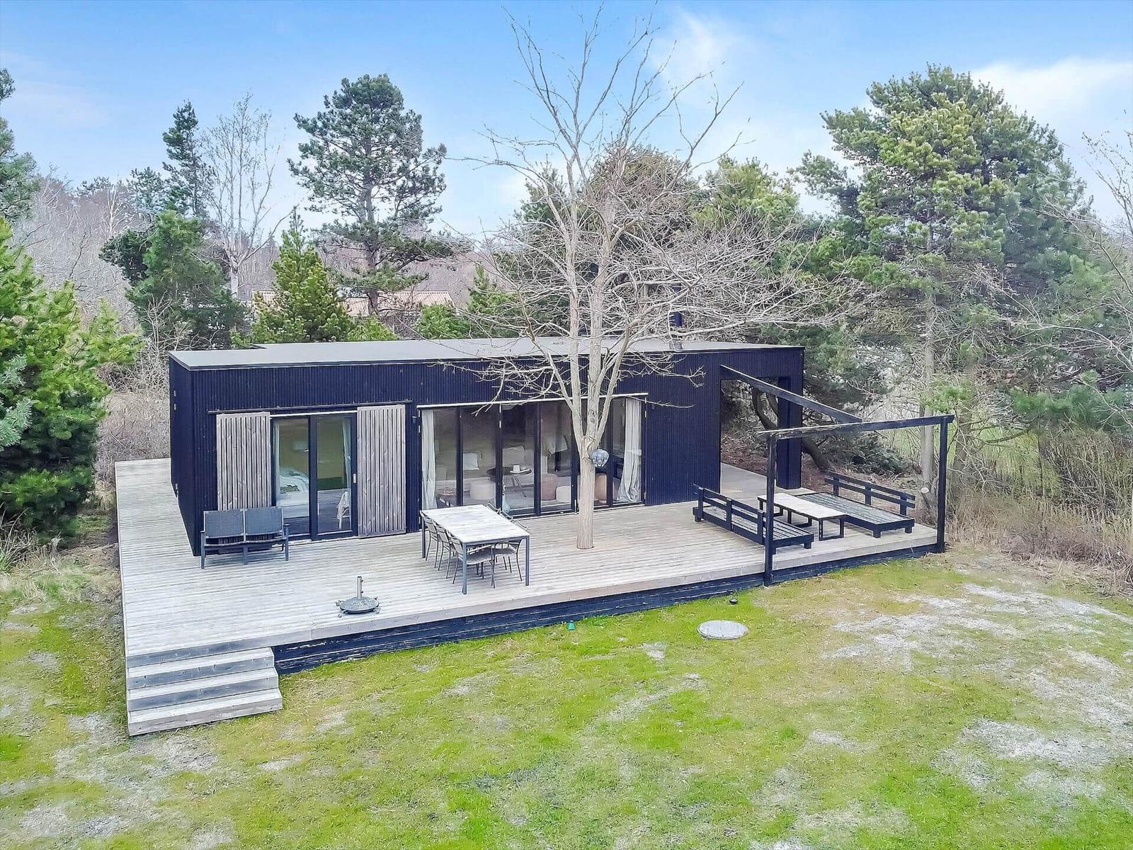 Moderne Hütte mit großem Holzterrasse, Garten und Bäumen umgeben.
