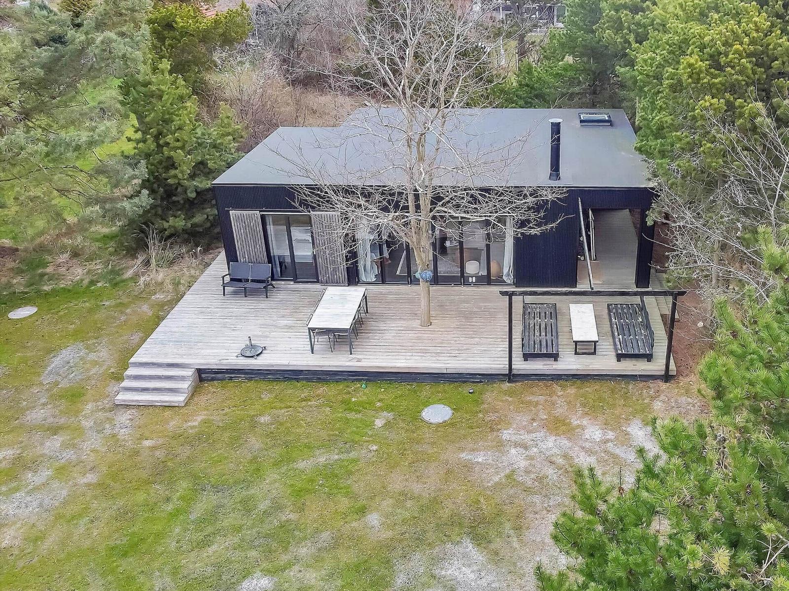 Moderne Hütte mit großem Holzterrasse, Grill und Sitzgelegenheiten im Wald.