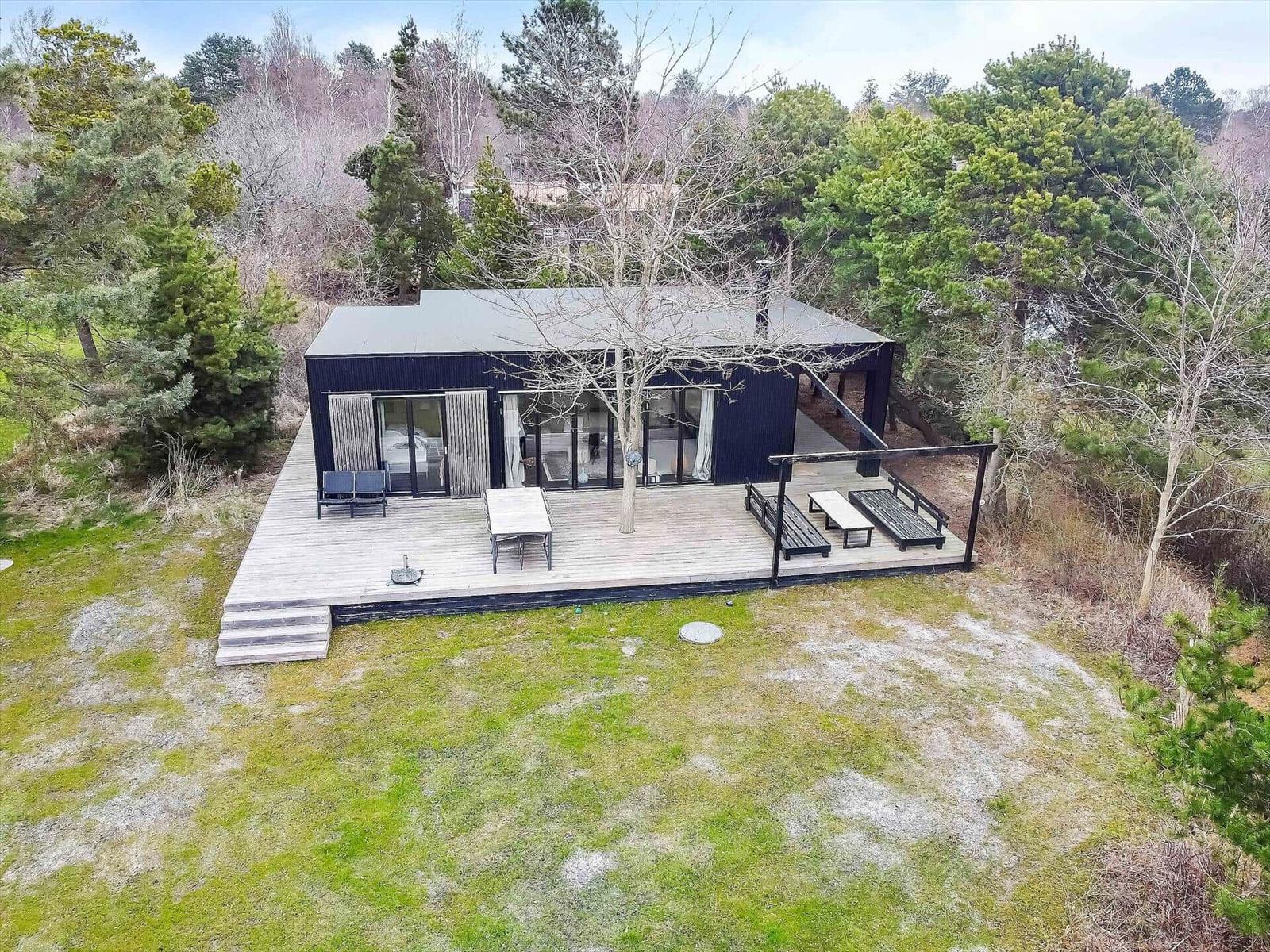 Moderne Hütte mit großem Holzdeck, Garten und Bäumen umgeben.