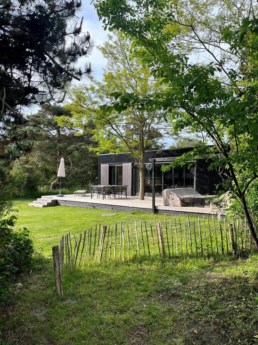 Moderne Villa mit Terrasse, Garten und Grillplatz unter Bäumen.