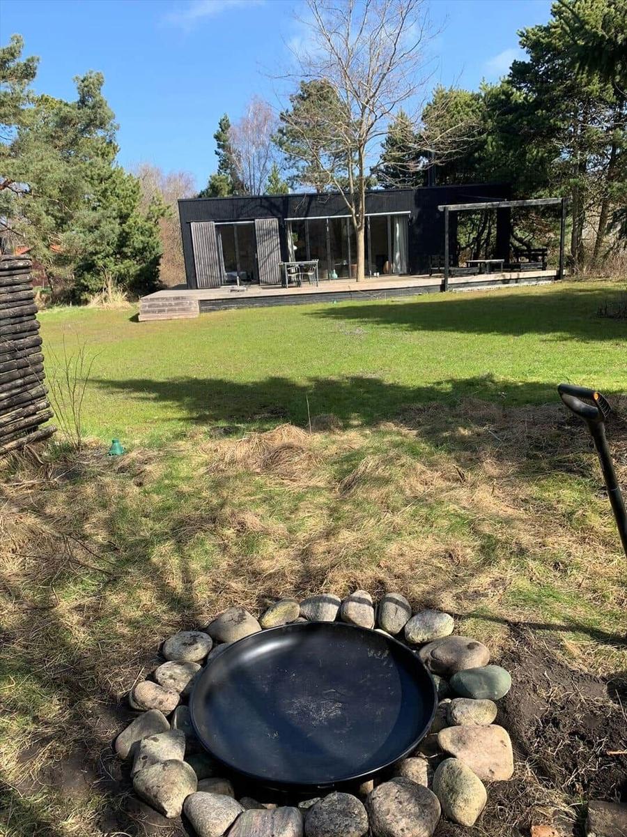 Haus mit Terrasse und Grillplatz im Garten. Grasfläche und Bäume umgeben die Anlage.
