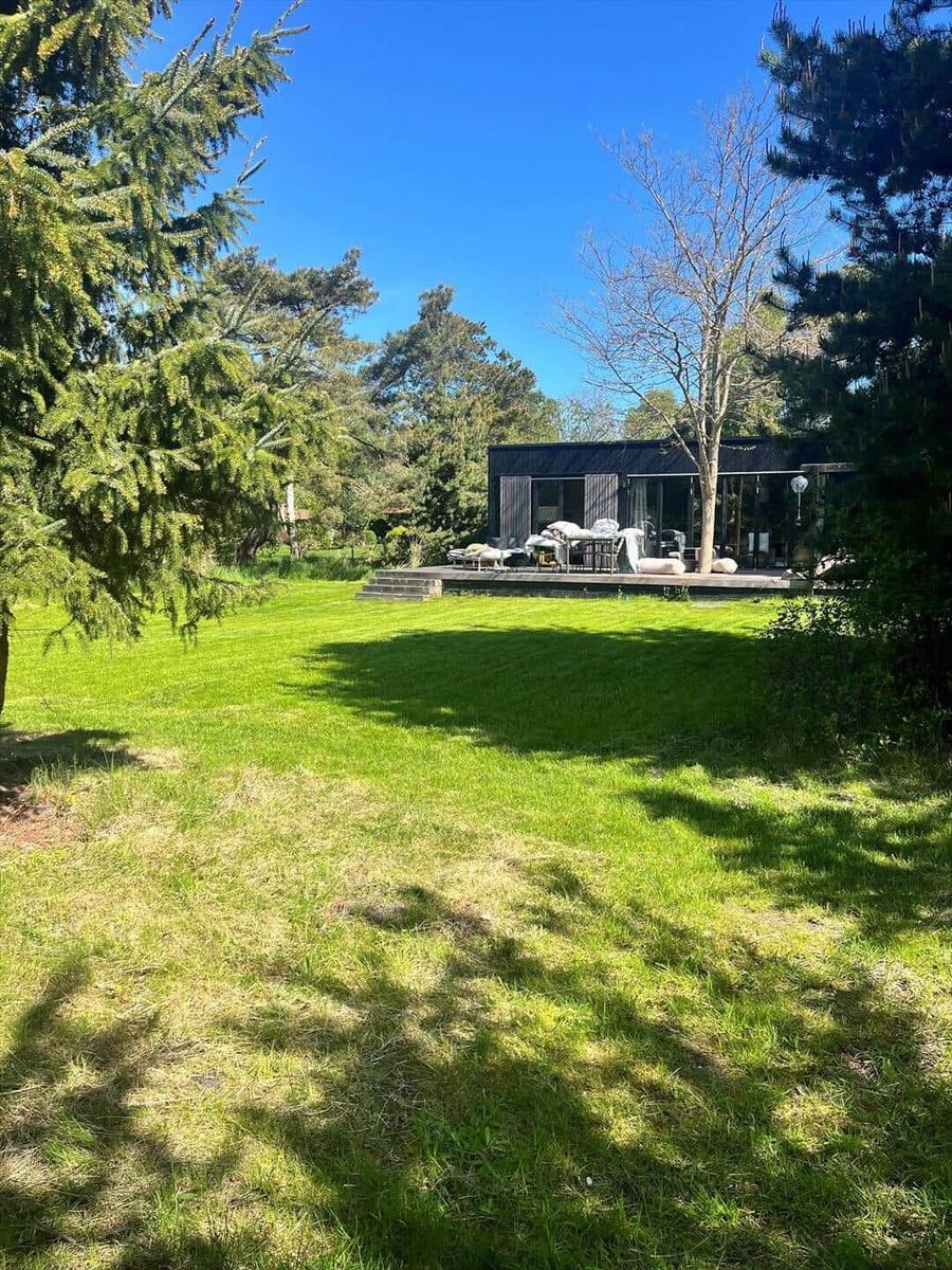Moderne Villa mit Terrasse und Garten. Umgeben von Bäumen unter blauem Himmel.