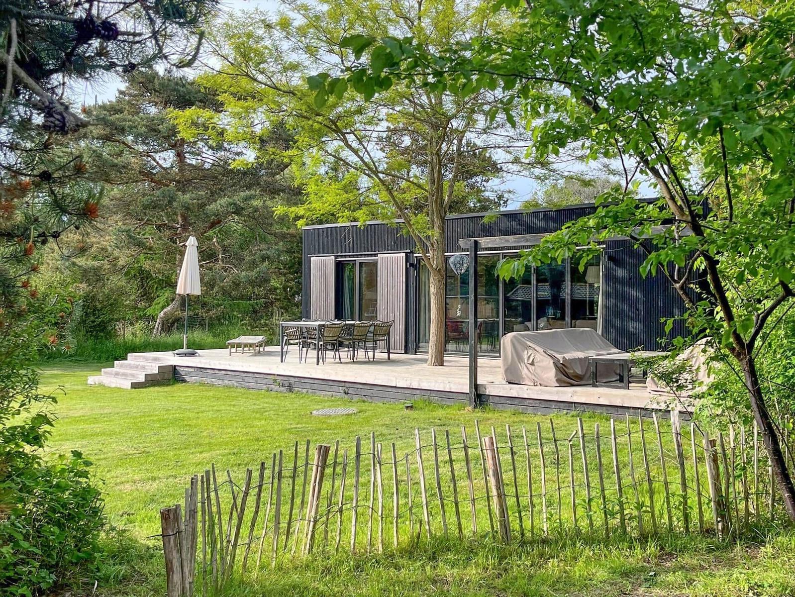 Moderne Villa mit Terrasse, Garten und Bäumen. Außentisch, Sonnenschirm und Grilldecke sichtbar.