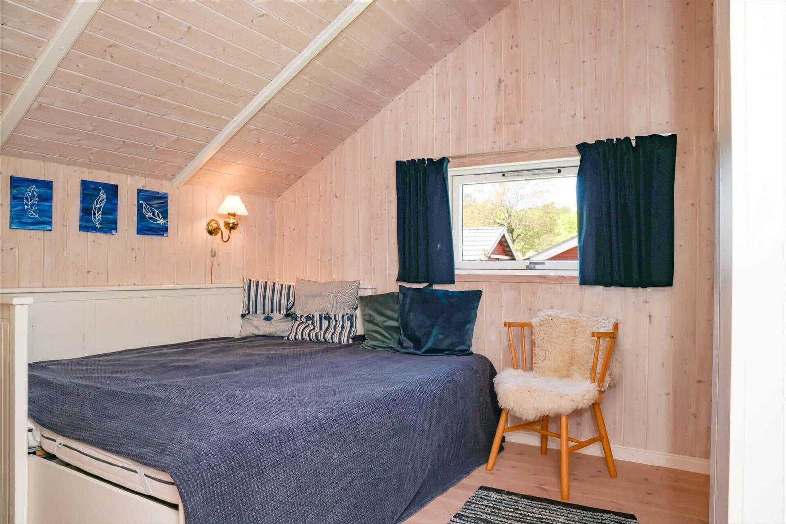 Bedroom with wooden walls, bed, chair, and window.
