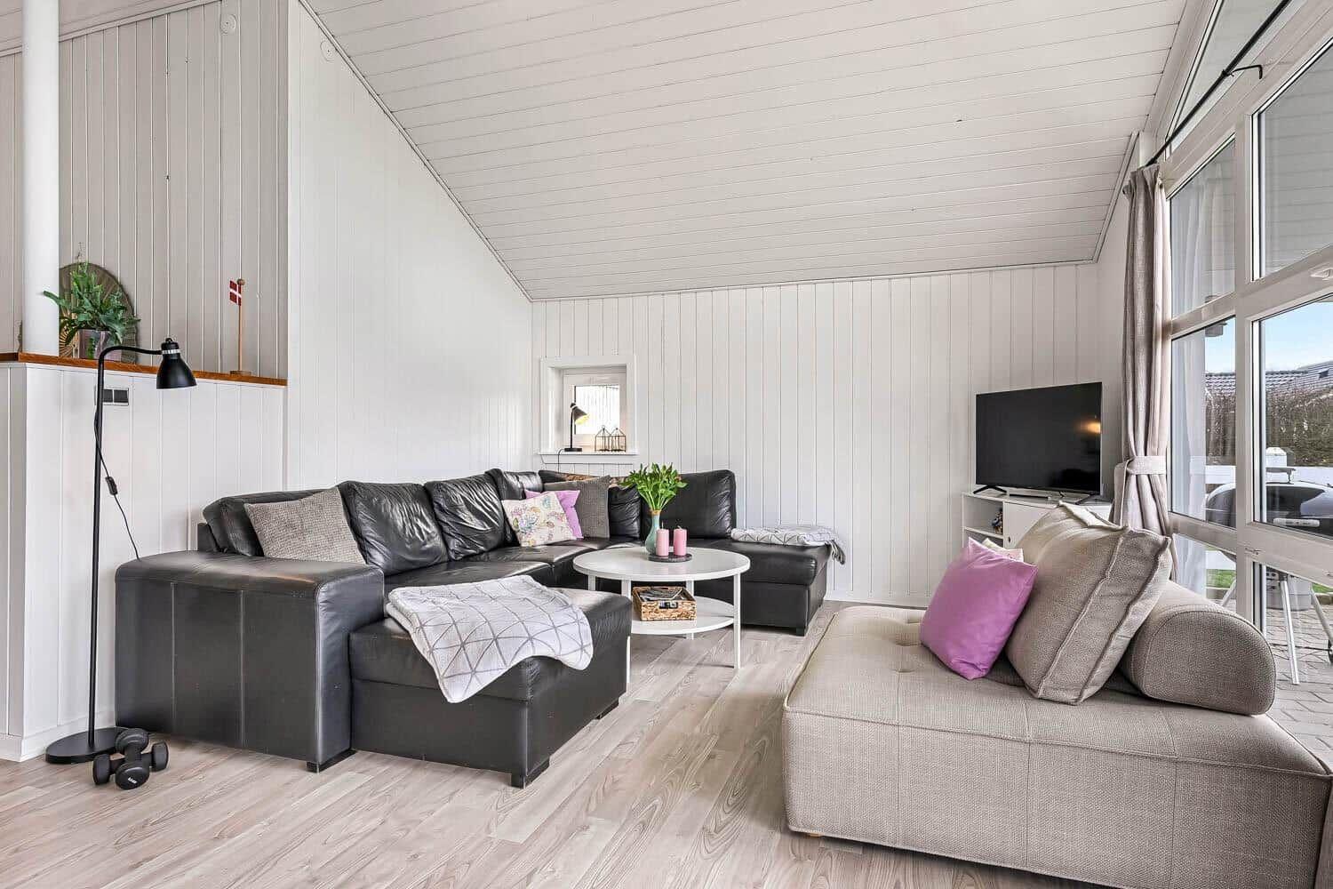 Wohnzimmer mit schwarzer Ledercouch, beigem Sessel und weißem Couchtisch.