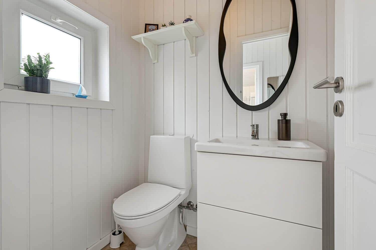 Badezimmer mit Toilette, Waschbecken und Spiegel an weiß verputzten Wänden.