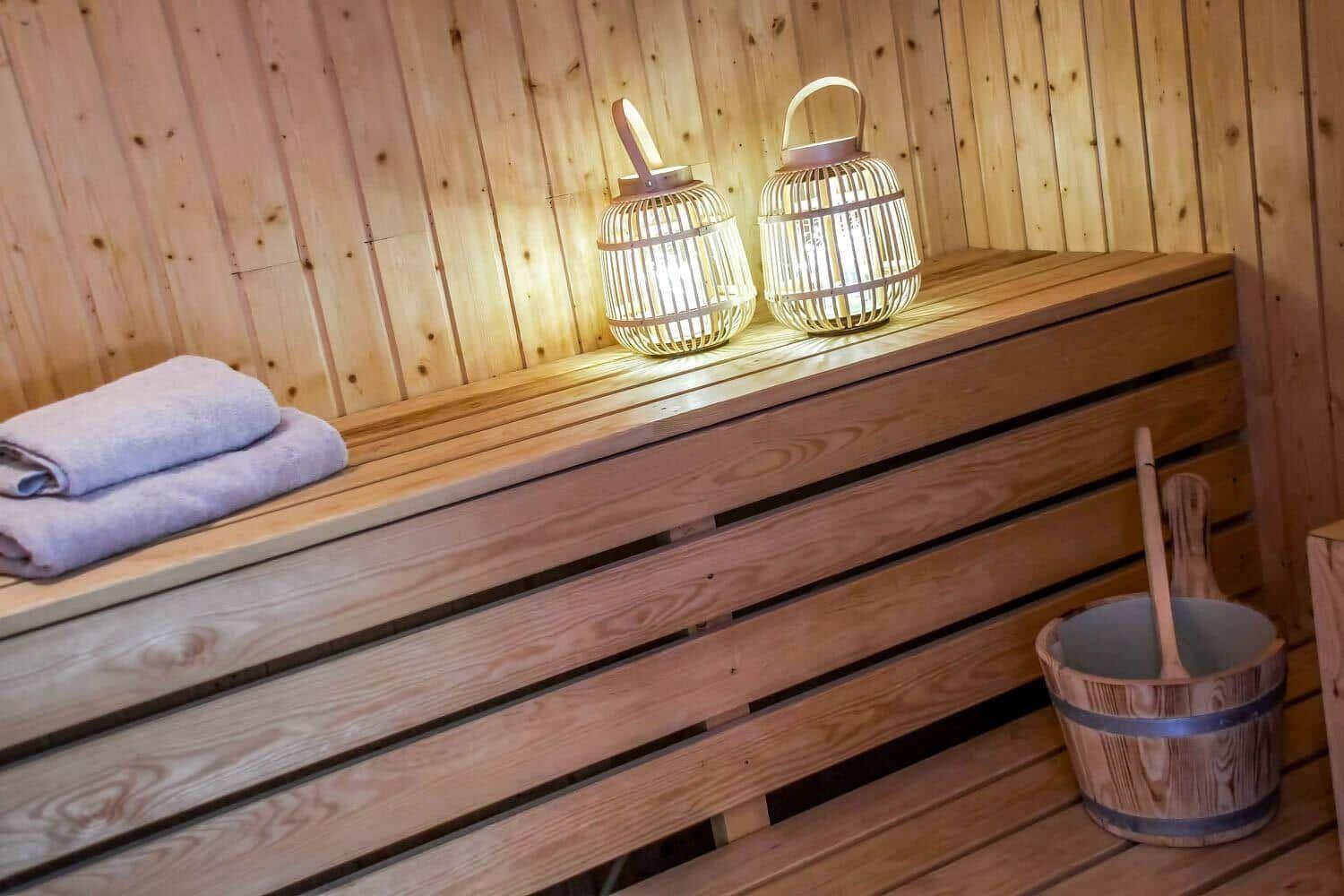 Sauna mit Holzbank, zwei beleuchteten Körben und einem Eimer mit Besen.