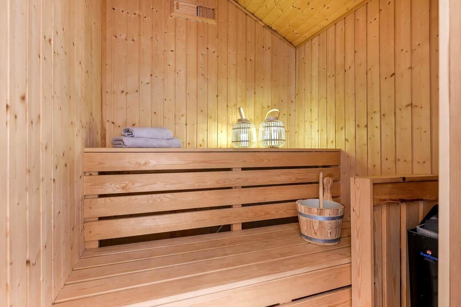 Holzsauna mit Bänken, gefalteten Handtüchern und einem Eimer mit Besen.