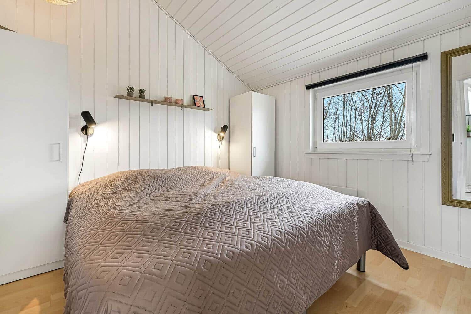 Schlafzimmer mit Bett, weißen Wänden, Fenster und Schrank.