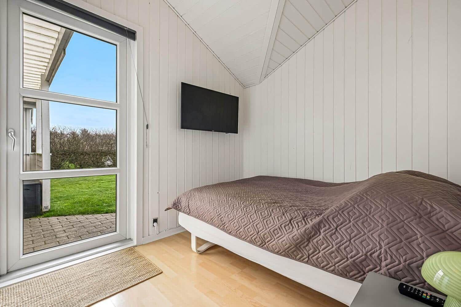 Schlafzimmer mit Bett, Fernseher und Fenster zum Garten.