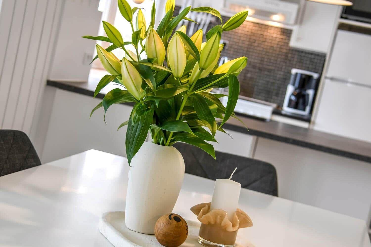 Auf dem Tisch steht eine weiße Vase mit gelben Lilienblüten und einer Kerze.