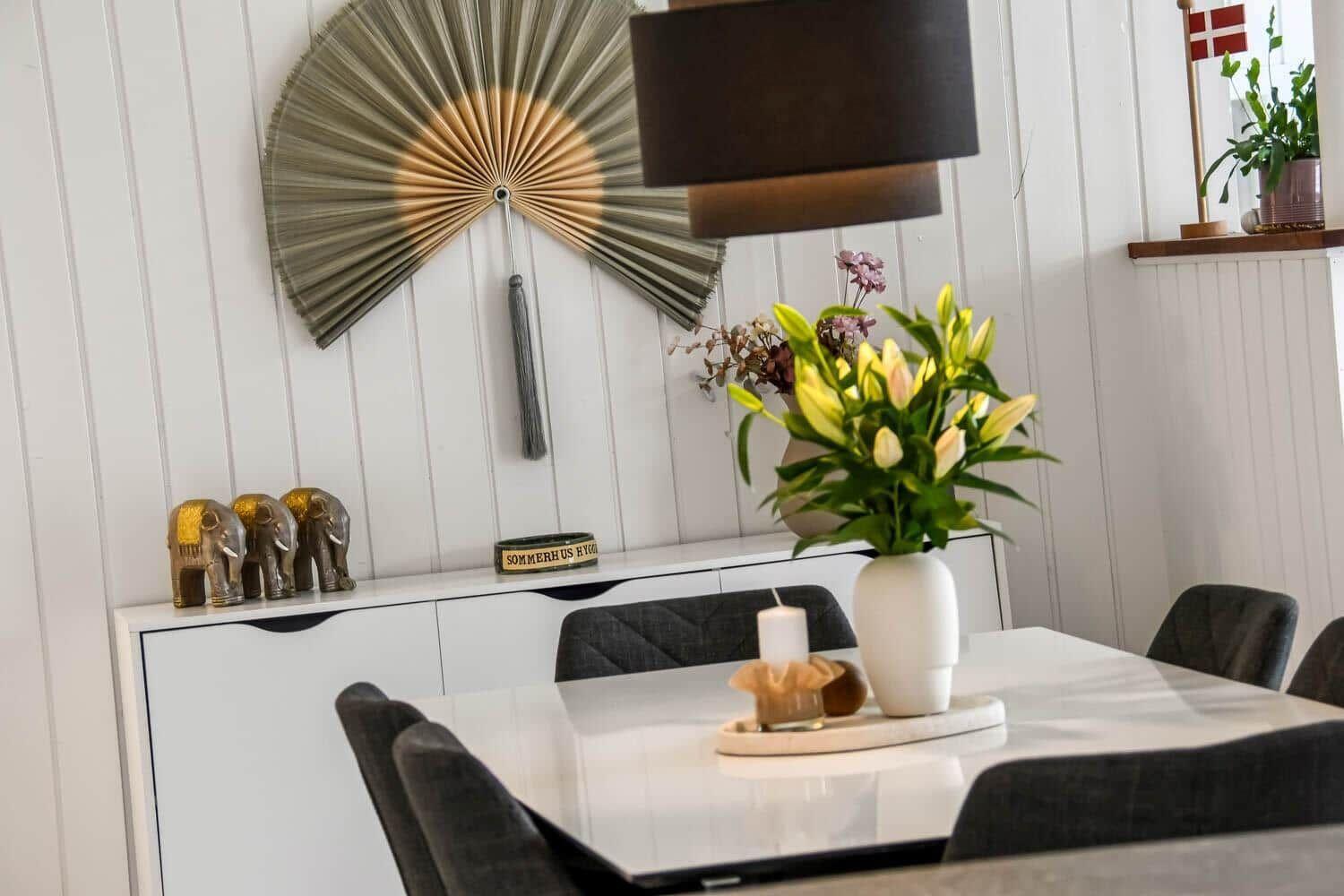 Esstisch mit Stühlen, Vase mit Blumen und Deko auf Sideboard.