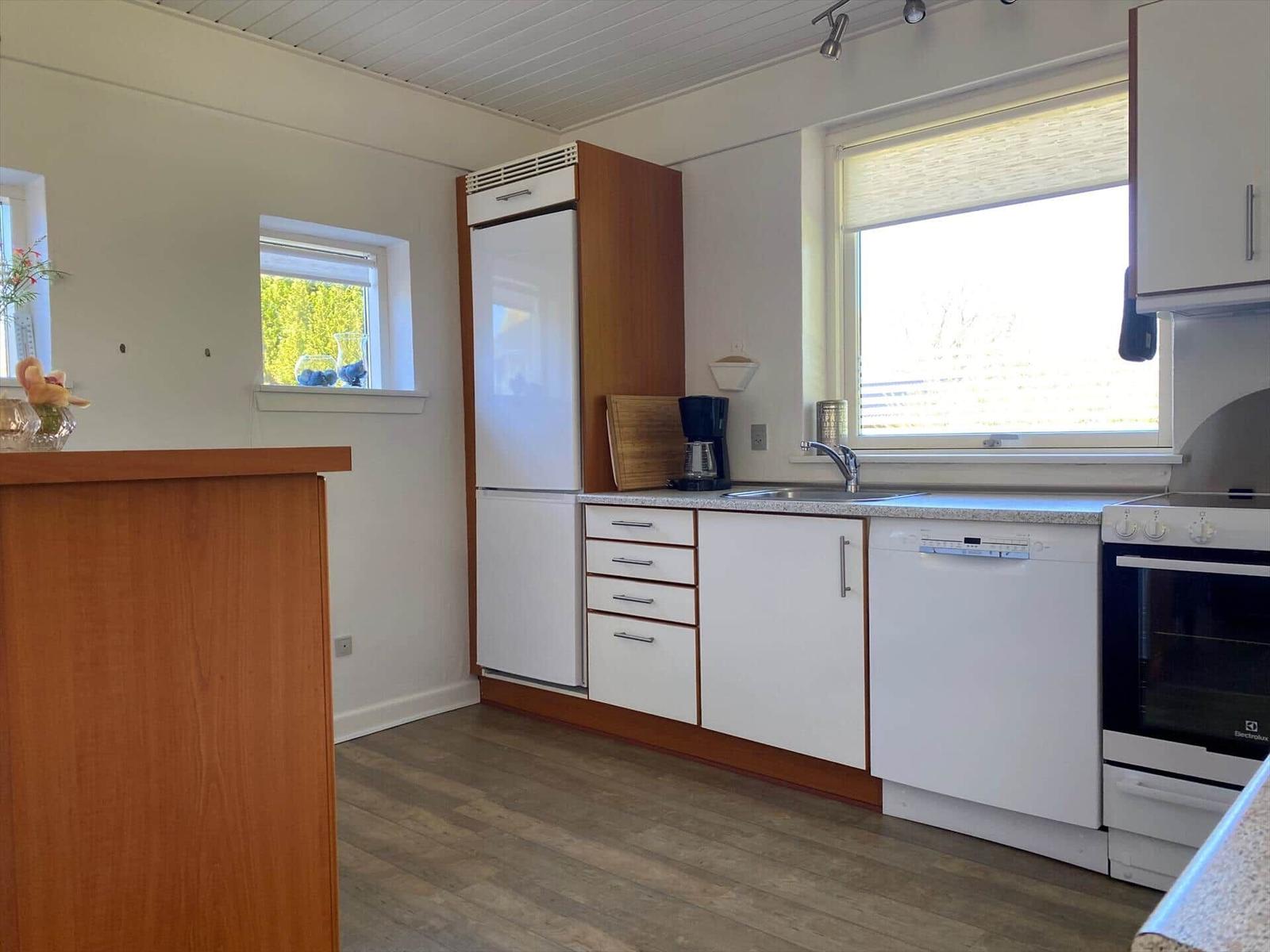 Küche mit weißen Schränken, Kühlschrank, Spüle und Fenster.