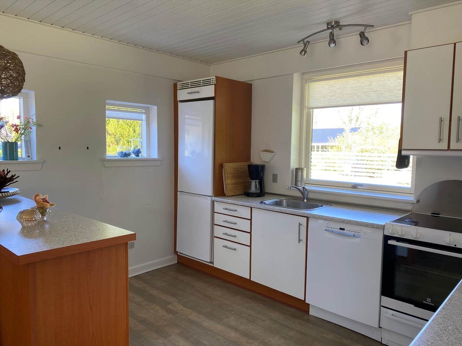 Küche mit weißen Schränken, Spüle, Kühlschrank und Herd. Holzoberfläche und Fenster.