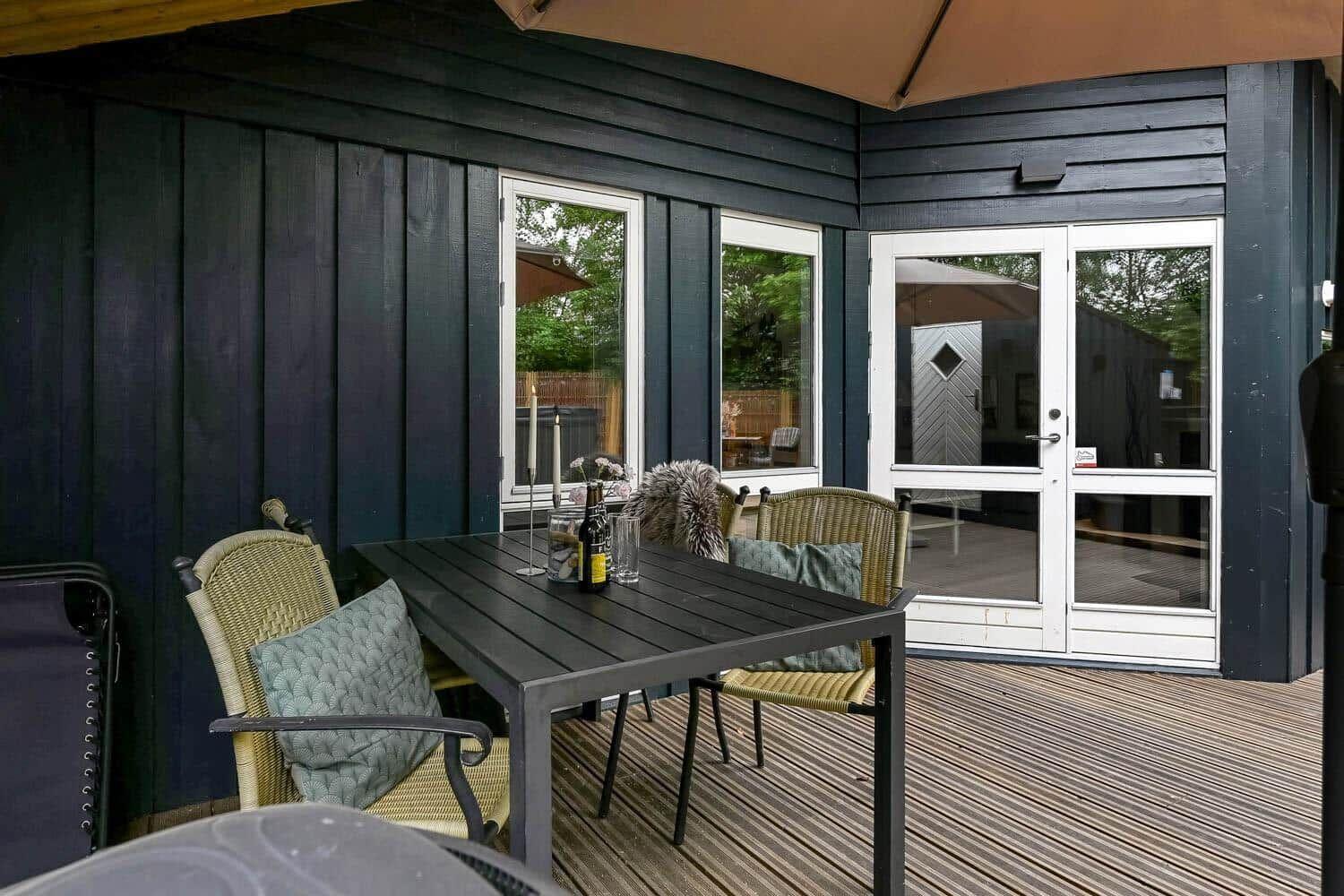 Terrasse mit Tisch, Stühlen und Sonnenschutz. Hintergrund: Haus mit Fenstern und Tür.
