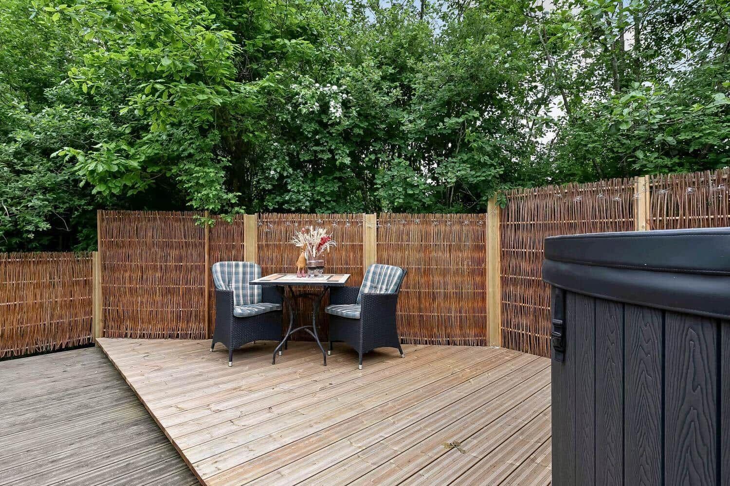 Holzterrasse mit Sitzgruppe und Whirlpool, umgeben von einer Bambuszaun.