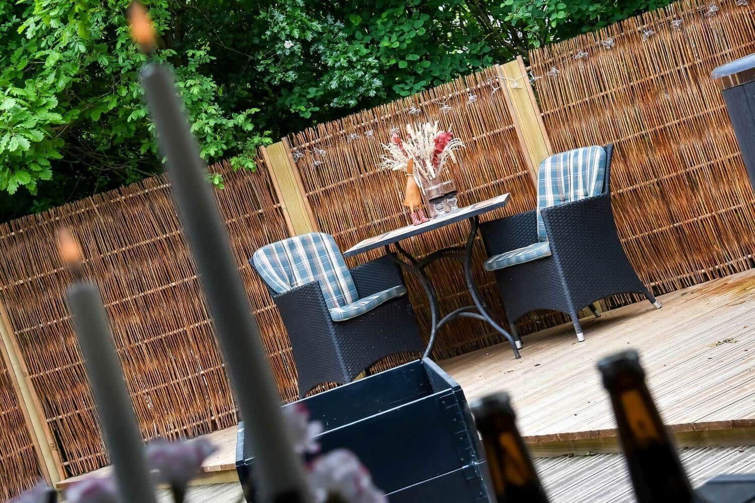 Terrasse mit Tisch, zwei Stühlen und Bambuszaun im Hintergrund.