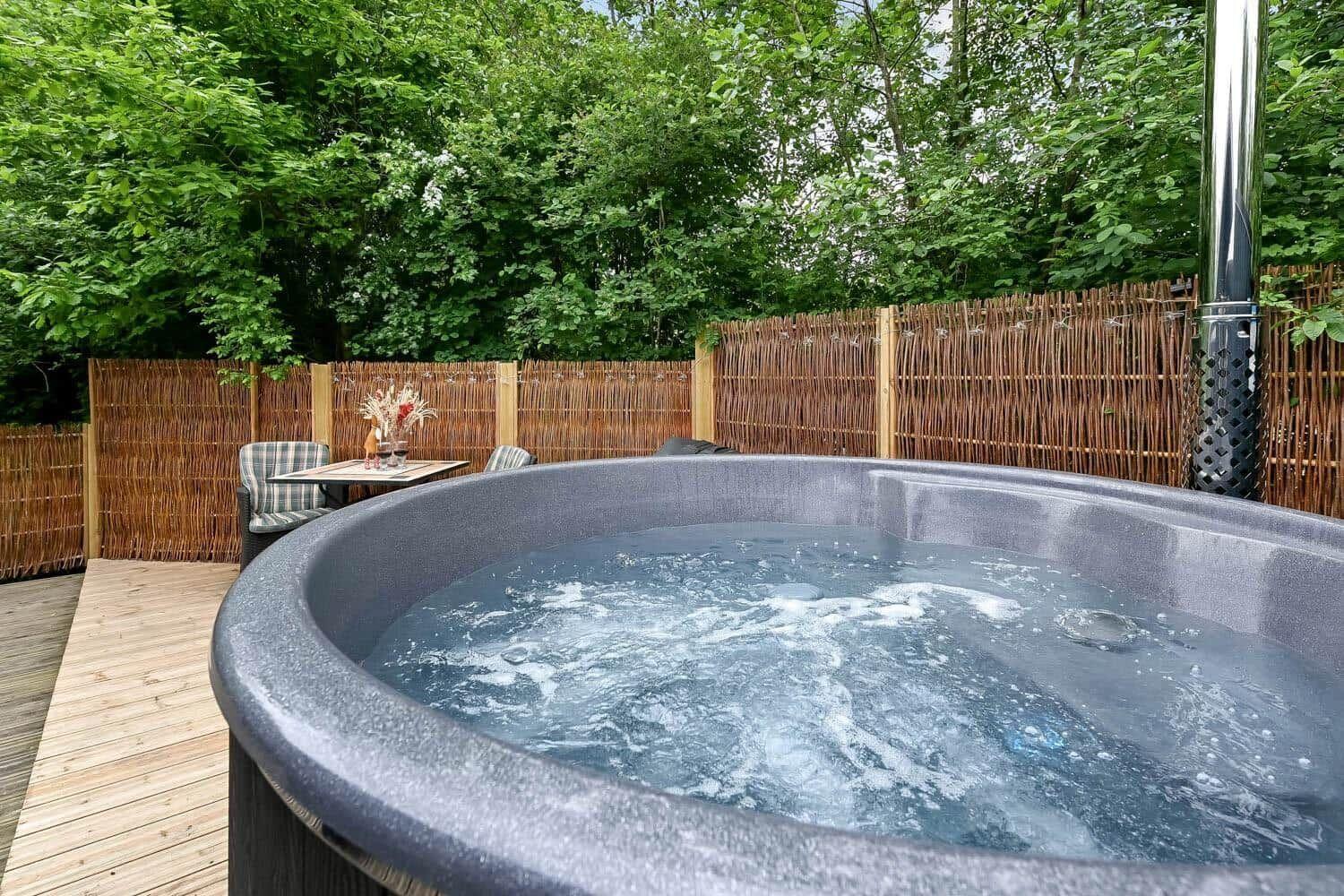 Ein Whirlpool auf einer Terrasse mit Holzdecke und Sitzgelegenheit hinter einem Bambuszaun.