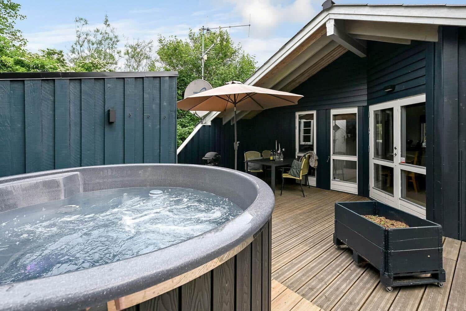 Hochwertiger Whirlpool auf Terrasse mit Sitzgruppe und Blick auf das Haus.