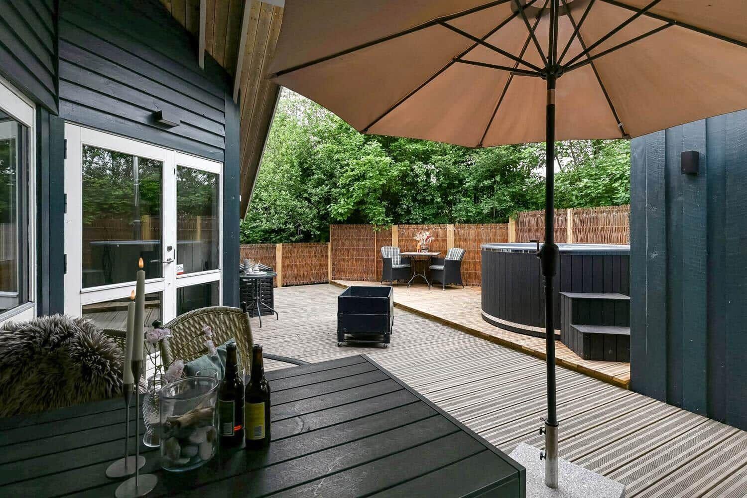 Terrasse mit Sitzgelegenheiten, Sonnenschirm und Whirlpool im Hintergrund.