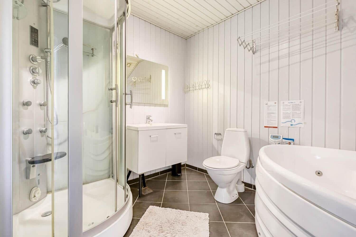 Bathroom with shower, toilet, and bathtub. White walls and dark floor.