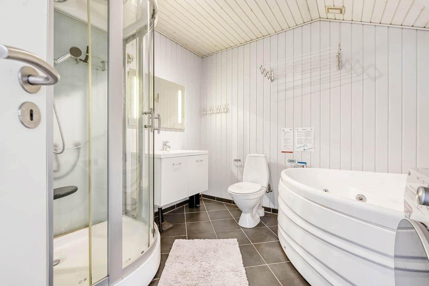 Bathroom with shower, bathtub, and toilet. White walls and dark floor.