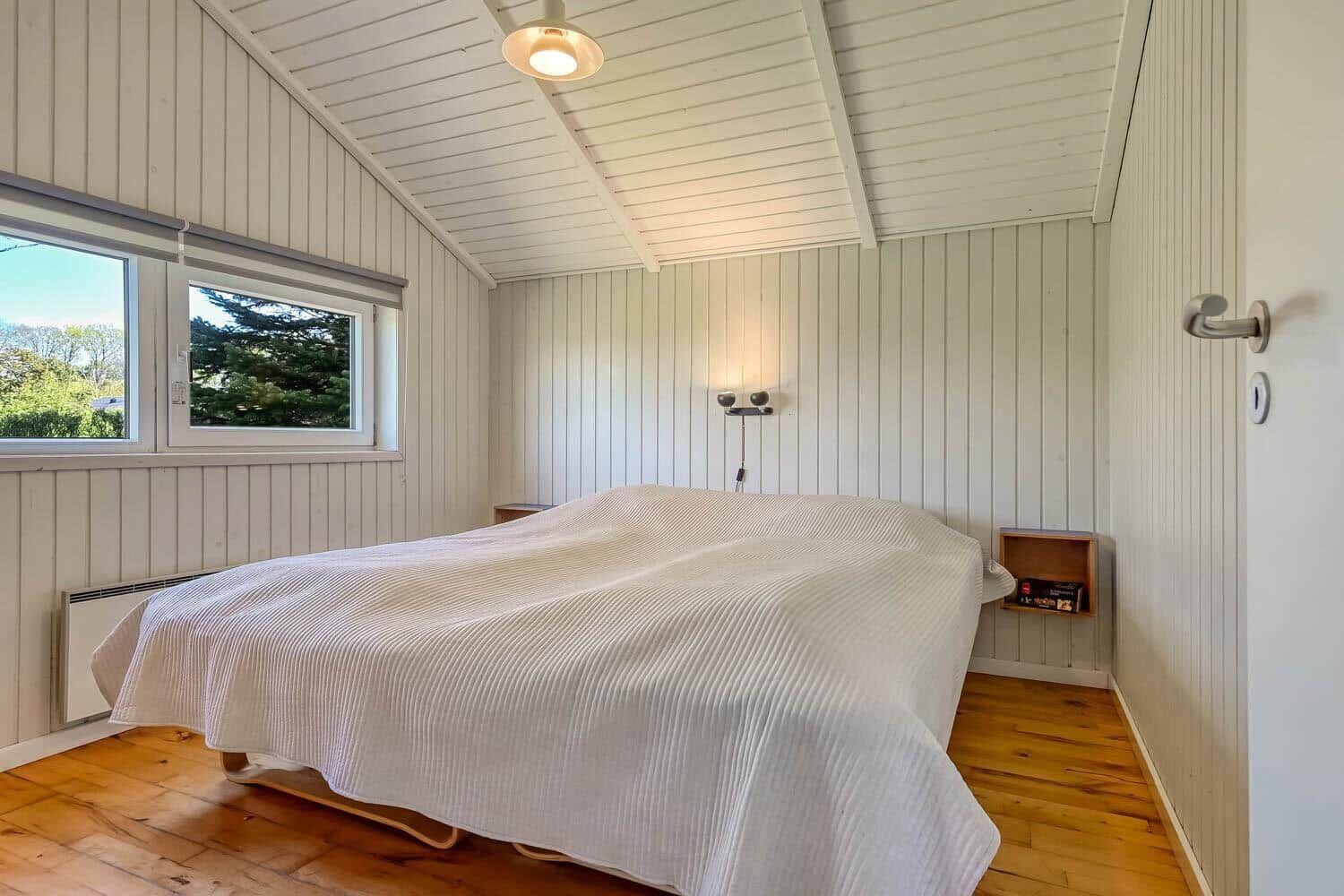 Bedroom with bed, wooden floor, and window. Ceiling with wood paneling and wall lighting.