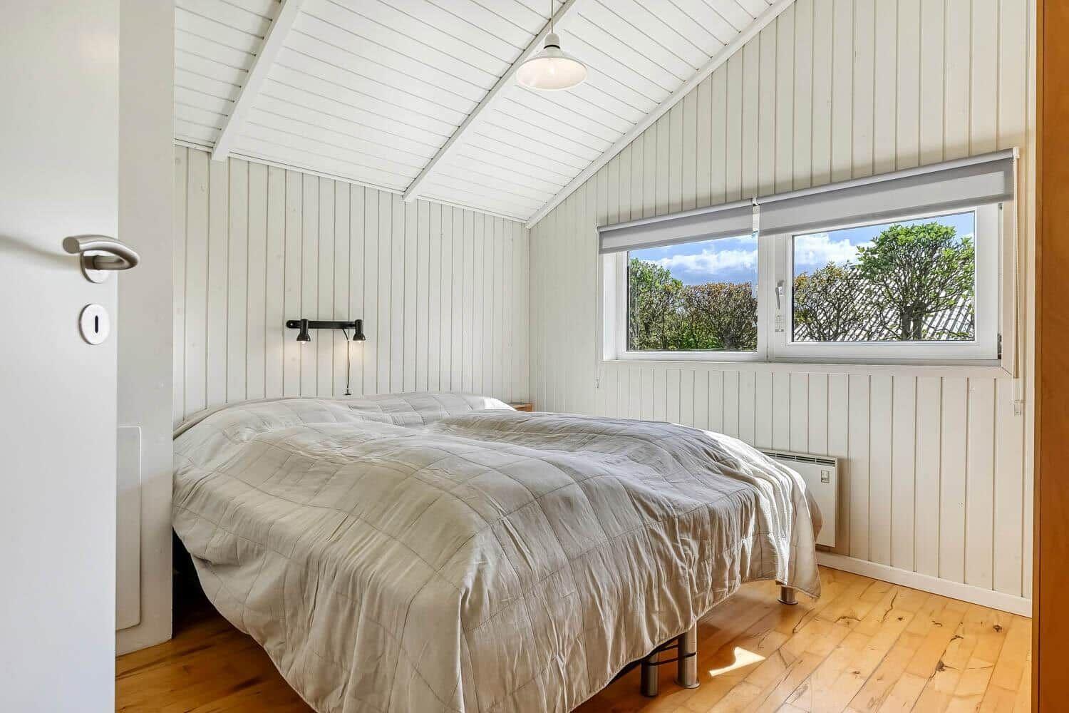 Bedroom with double bed, wooden floor, and window with view of trees.